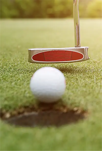 golf ball on the edge of the hole about to be tapped in by putter