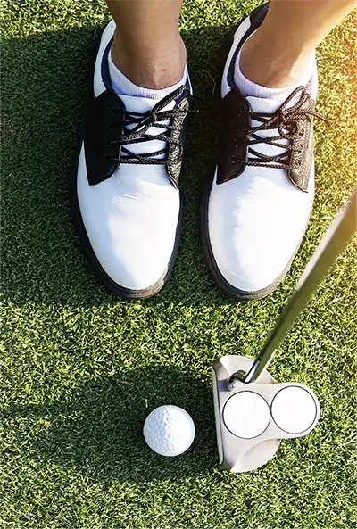 downward view of golfer's shoes and putter next to a golf ball
