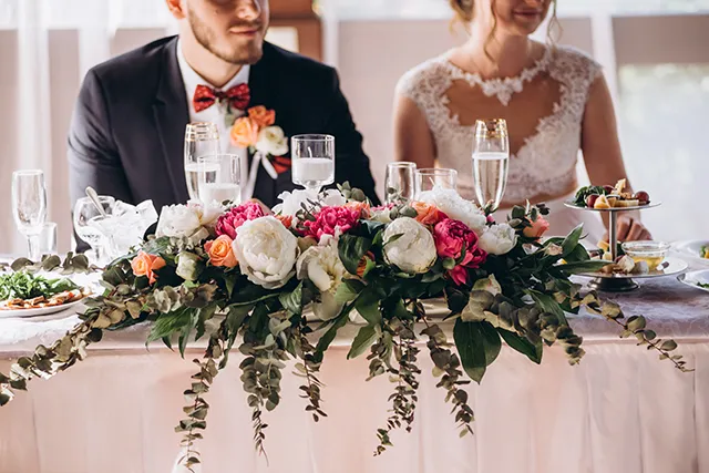 A bride and groom sit at table catered with food and drinks